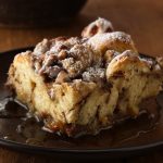 French Toast Casserole: A golden-brown baked dish with layers of fluffy bread cubes soaked in a rich custard, topped with a buttery streusel and dusted with powdered sugar, served with fresh berries and maple syrup.