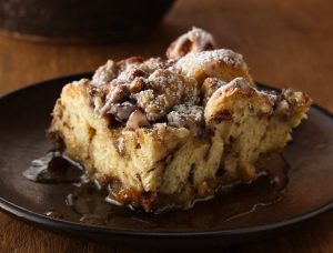 French Toast Casserole: A golden-brown baked dish with layers of fluffy bread cubes soaked in a rich custard, topped with a buttery streusel and dusted with powdered sugar, served with fresh berries and maple syrup.